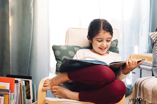 smiling little girl reading sitting at home, concept of leisure at home for children