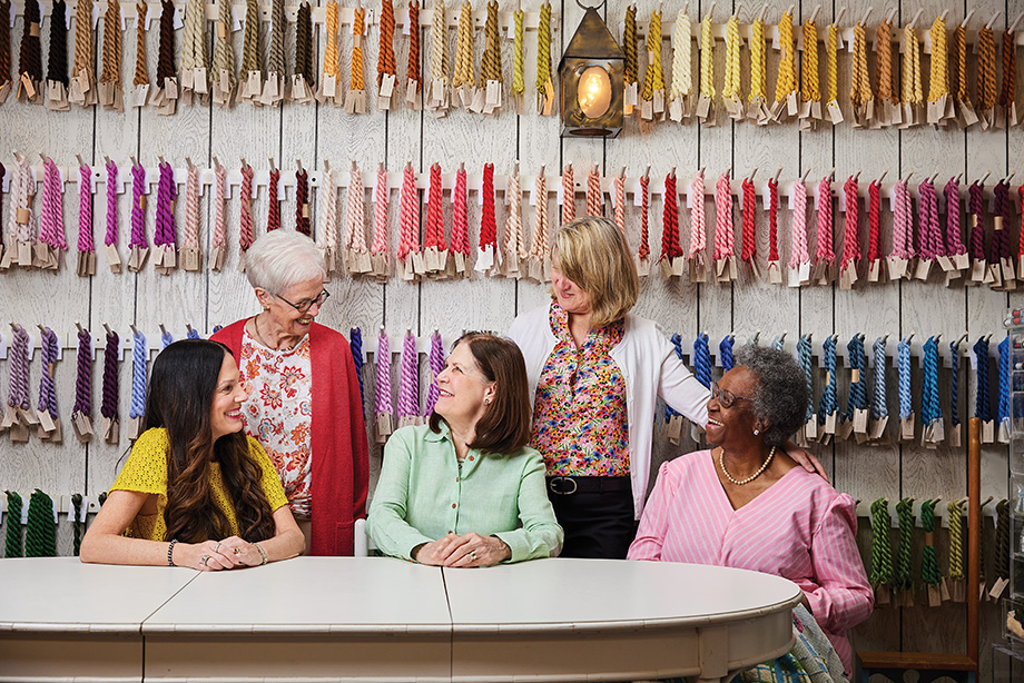 Molly Burns, Betsy Larson, Ginny Mahoney and longtime staff members Maureen Monchamp and Sandra Mitchell in front of a portion of the yarn selection at The Picket Fence.
