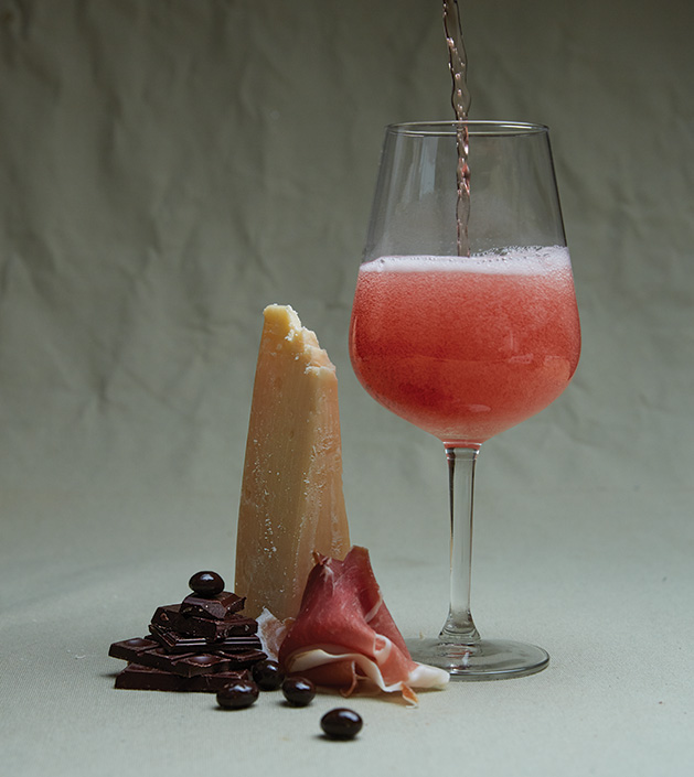 Assortment of chocolates, block of cheese and glass of pink wine.