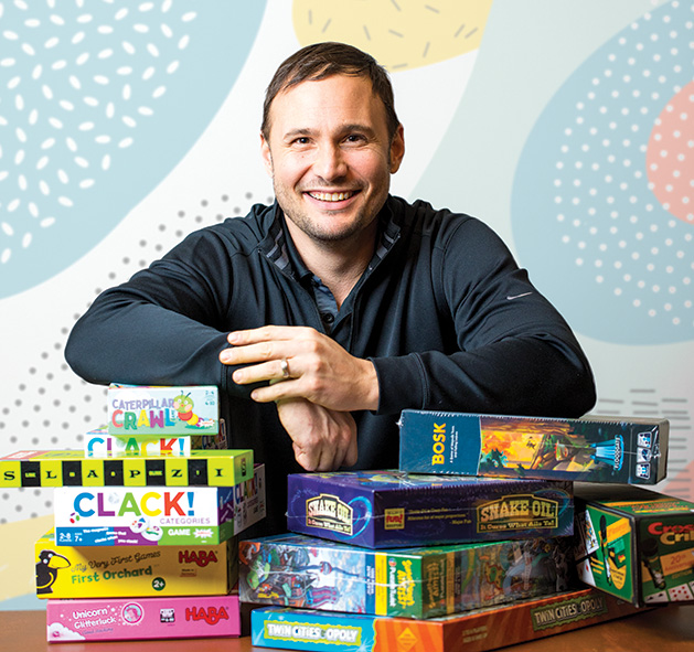 Games by James Edina owner Logan McKee sits behind some of his favorite board games.