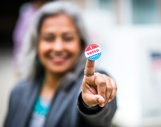 A member of the League of Women Voters holds up an "I Voted" sticker.