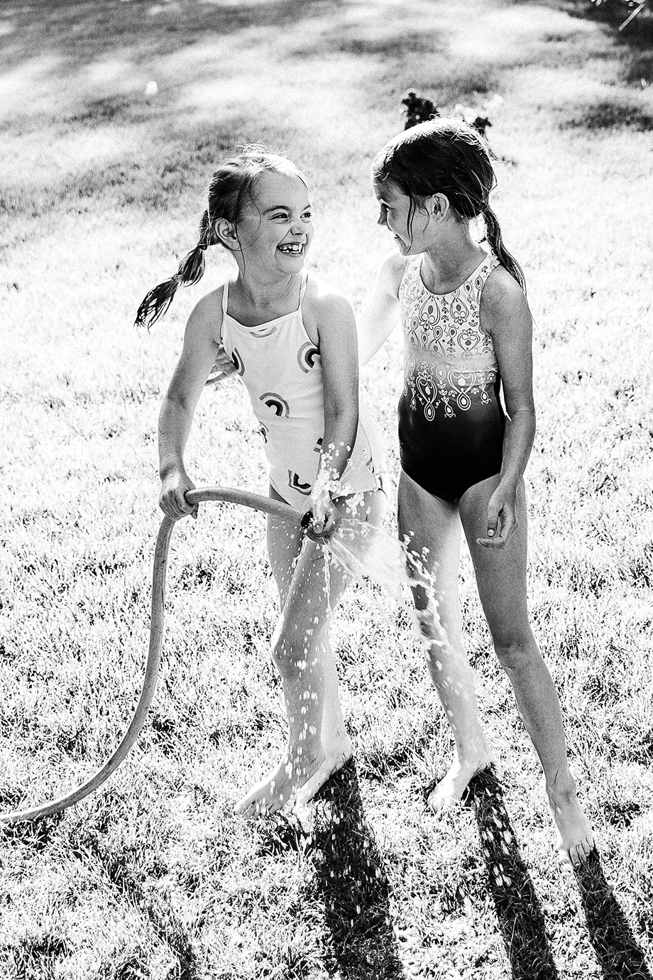 Two young girls playing outside with a garden hose.