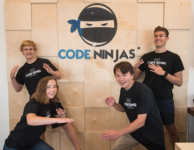 Four kids who learned coding through the Code Ninjas program pose in front of the logo.