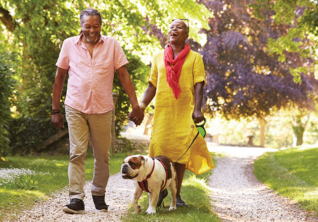 Two senior citizens walk with their pet dog. 