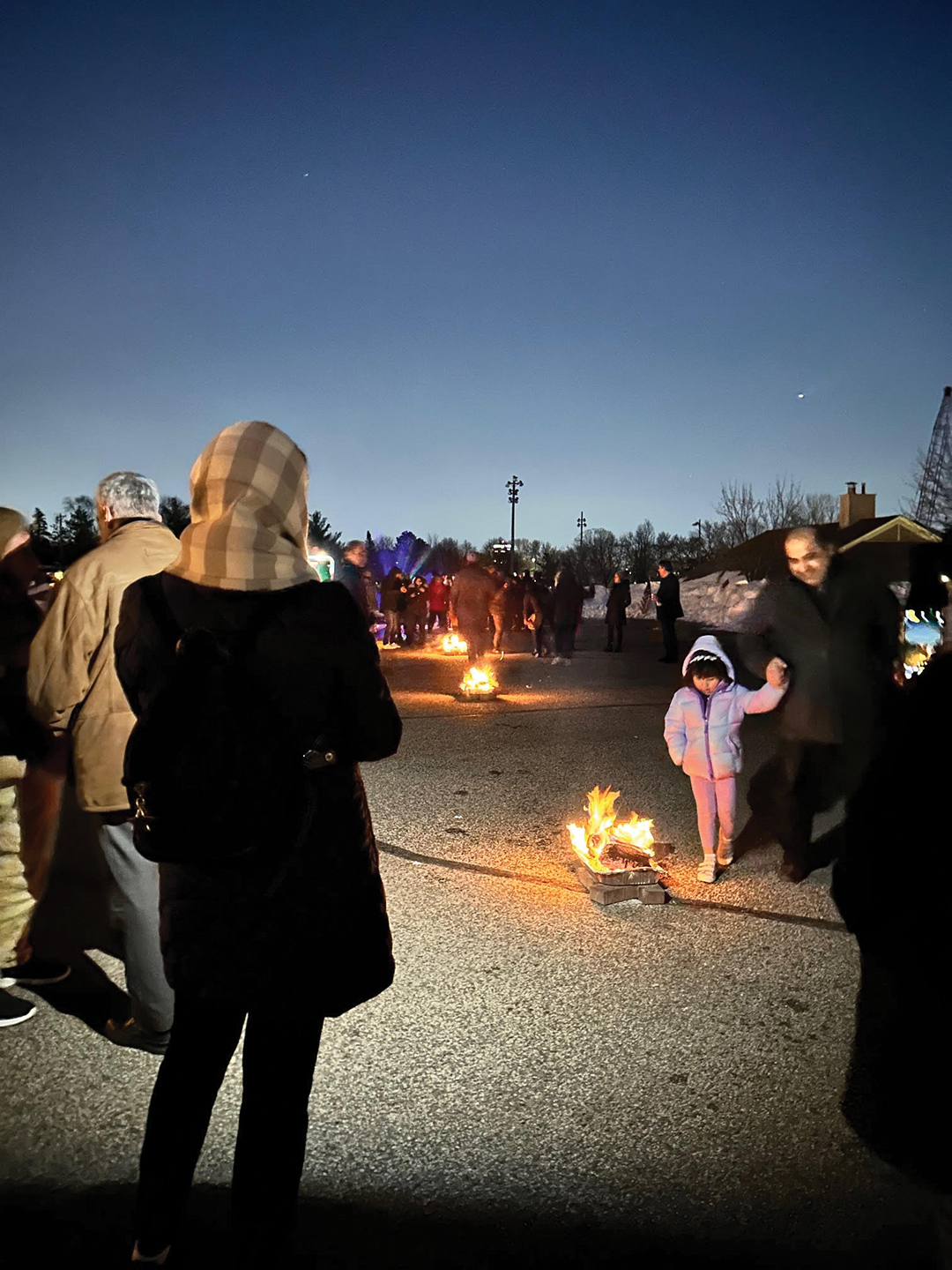 A woman watches a young girl jump over the fire at the 2023 Chaharshanbeh Suri event.