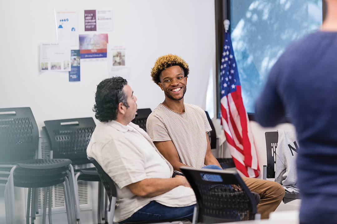 The smiling young adult male veteran listens to advice from the mature adult male therapist.