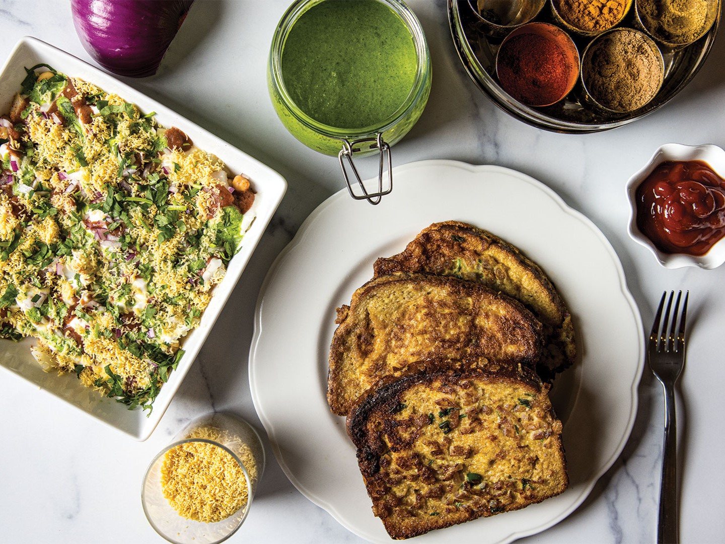 Savory French Toast sits amid a pot of chutney and a spice box or masala dabba.