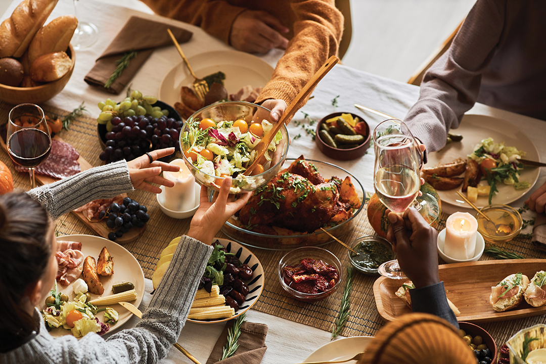 Multiethnic group of people at festive dinner table celebrating Thanksgiving together and enjoying rustic roasted dishes, copy space