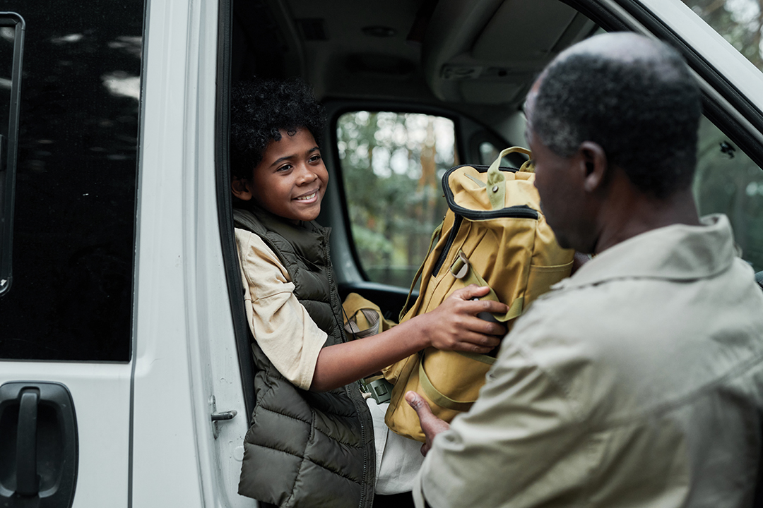 Little boy helping his dad to unloading bags from car for camping in the forest
