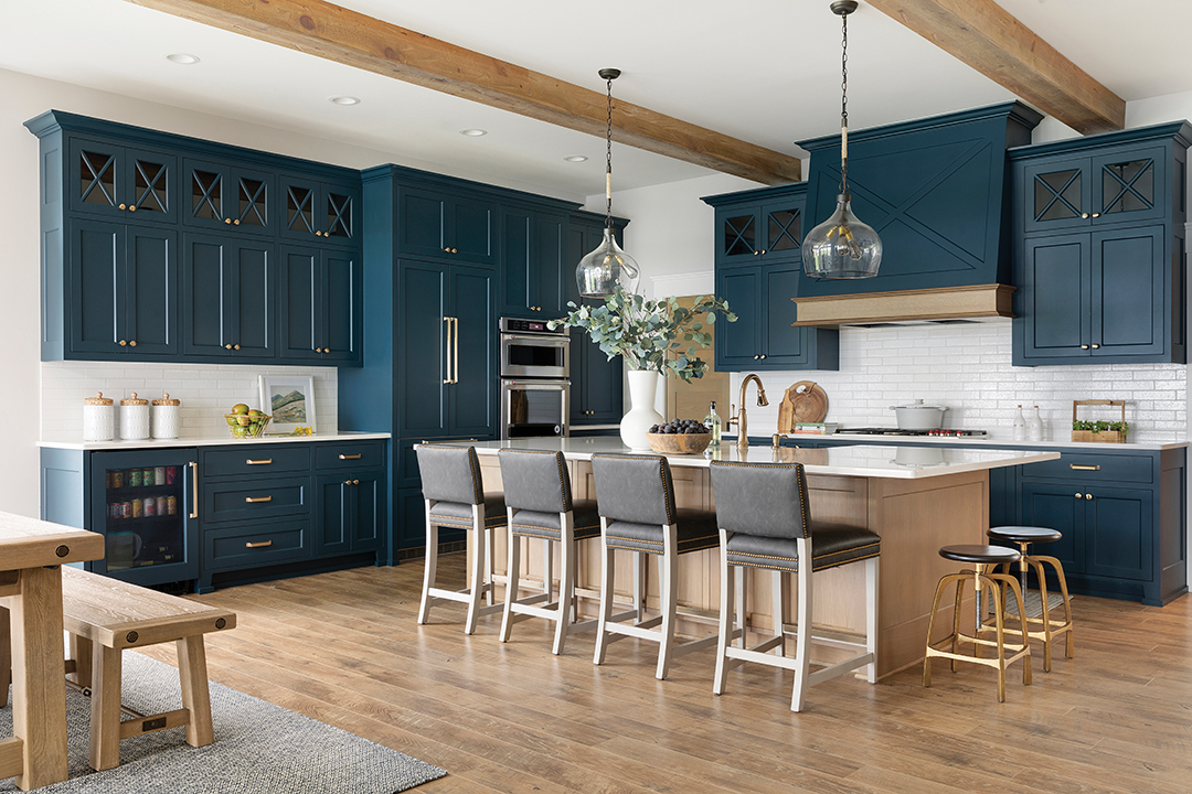 Designer Bhavana Bhimavarapu says that the owners have a deep love of water and they asked that the color blue be incorporated into the lake home’s kitchen. “We picked a color that works harmoniously with the lake outside,” Bhimavarapu says. She prioritized cleanable, durable and low-maintenance materials throughout the lake home. “The counter stools are finished in high-quality faux leather for added resilience … For the flooring, we chose matte engineered hardwood throughout the main living areas for reliable, long-term performance,” she says. Right: In contrast, the primary residence’s kitchen is white with gold accents.