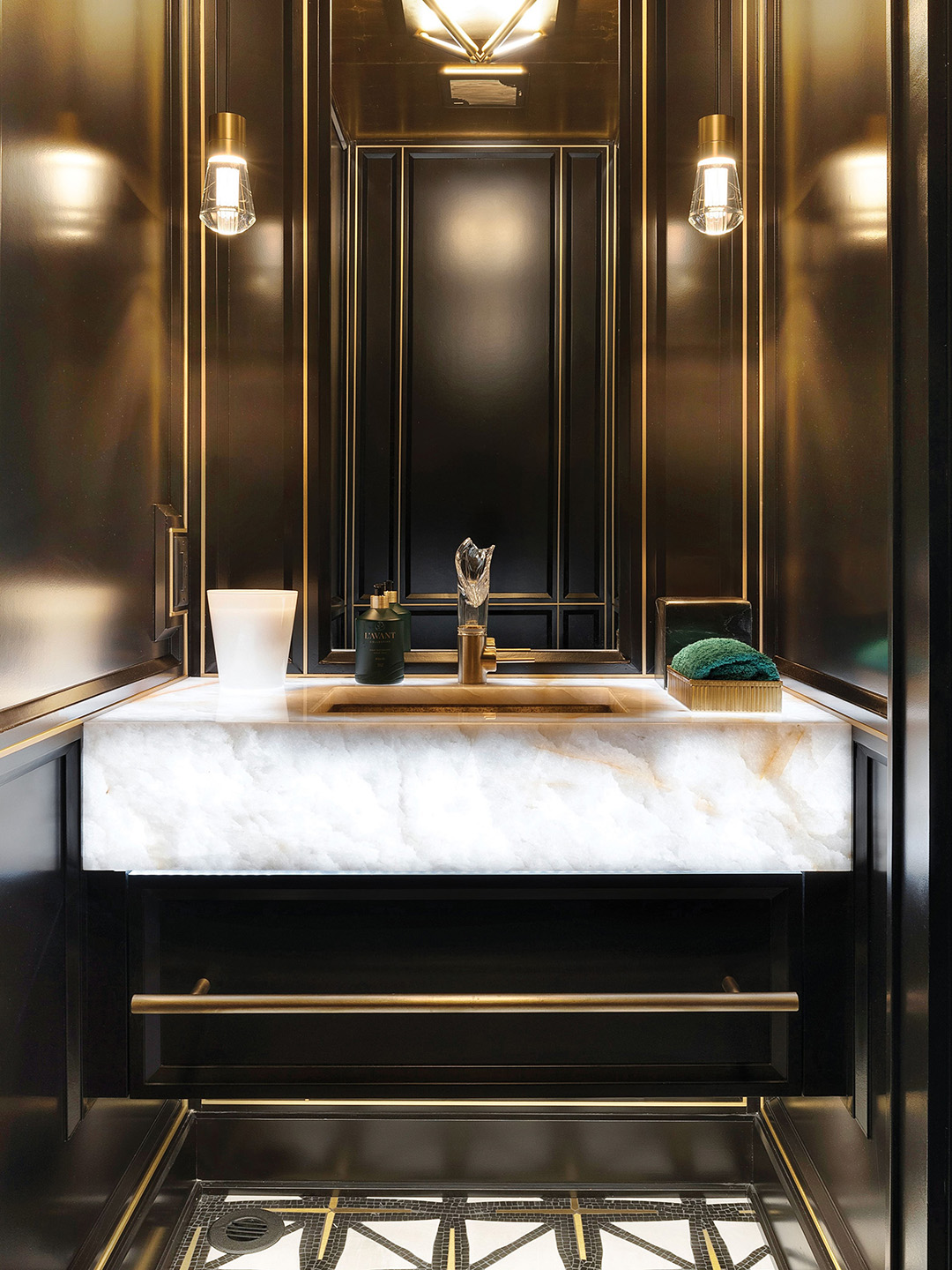 The powder room has black lacquered walls, marble floors, a brass sink and an imported German crystal faucet. The look is elevated with a Kelly green towel.