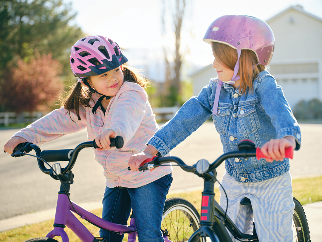 Two young girl friends riding bicycles together in a neighborhood.