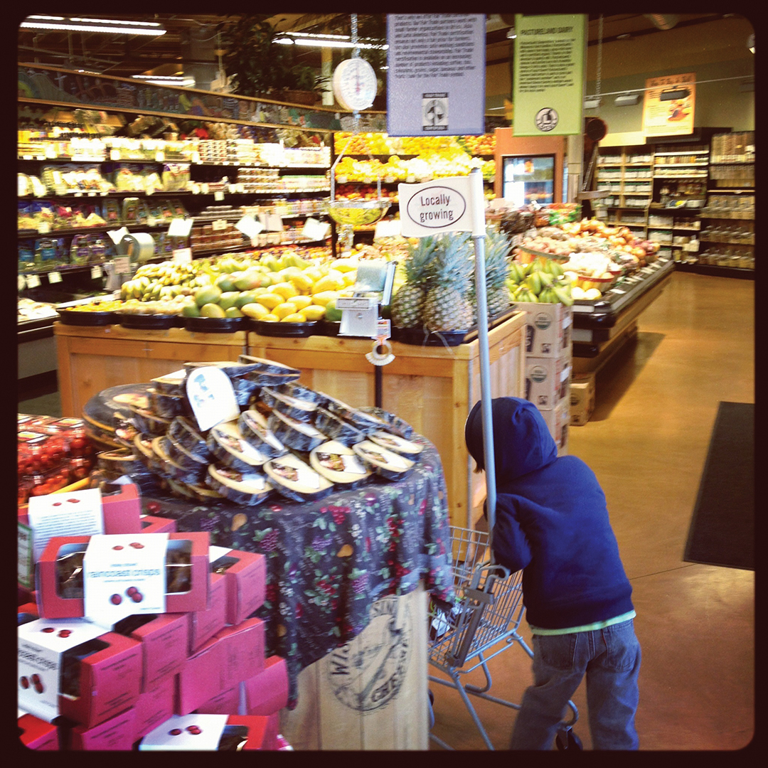 In this photo, taken by Heier, a younger Alex pushes a miniature shopping cart through the store. Its small flag reads, “Locally Grown.” Heier says the phrase feels especially fitting for her family, given how closely their routines and memories are tied to the co-op and the neighborhood.